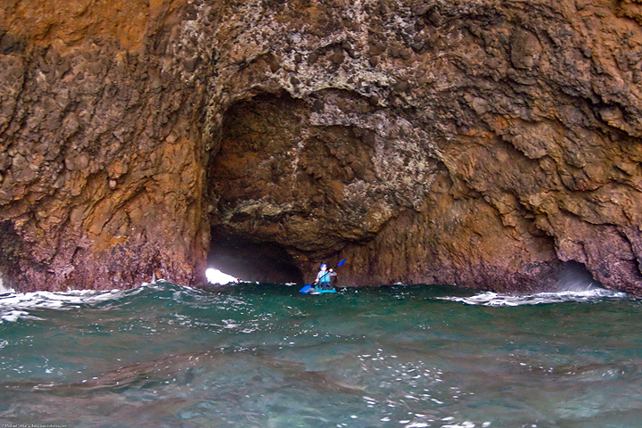 kayaker emerging from tunnel made by arched rock